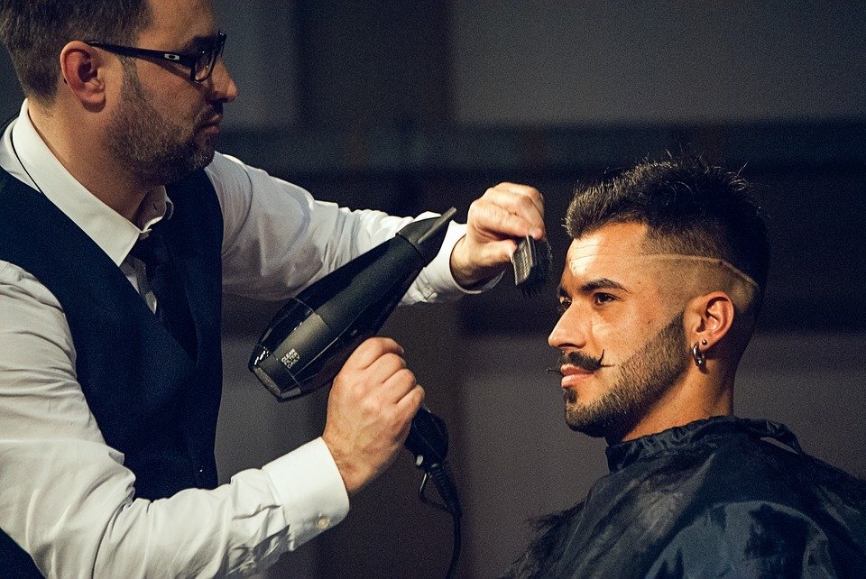 Seorang pria sedang dipotong rambutnya oleh seorang barber di salon